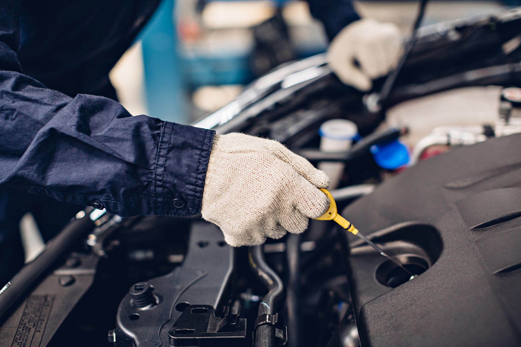 Auto car repair service center. Mechanic checking engine oil level.