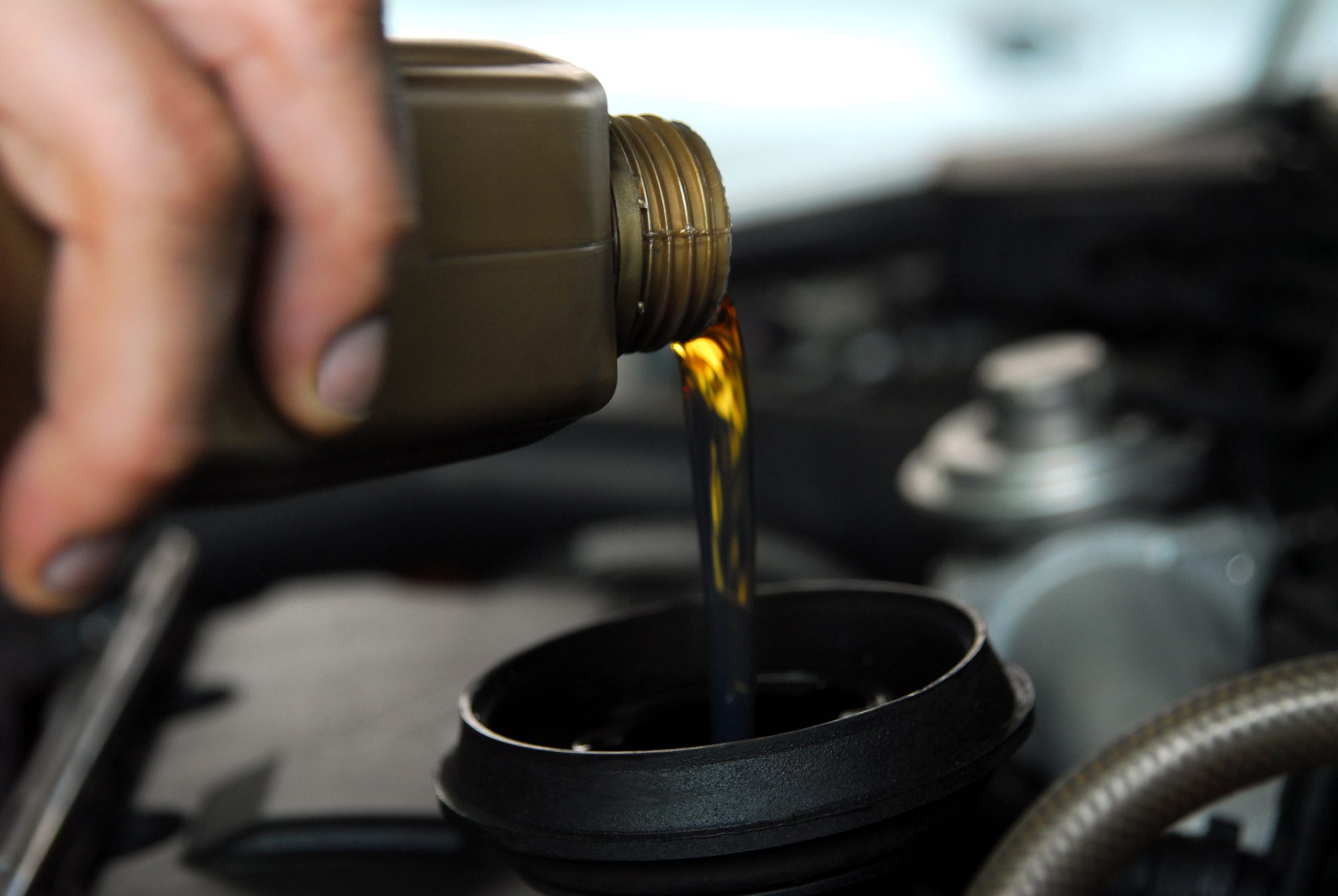 Man s hand holding a bowl of motor oil and poured into the engine