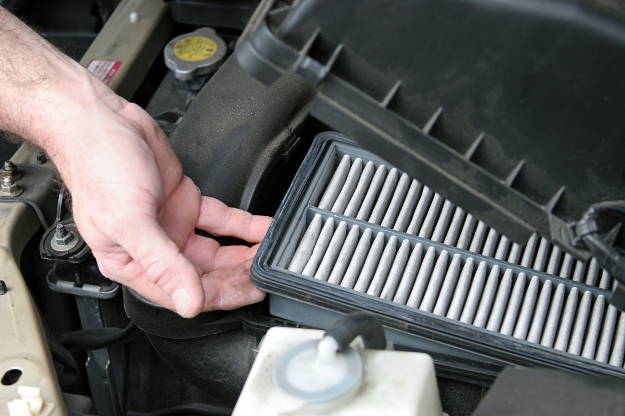 An auto mechanic removing the dirty air filter from an automobile.