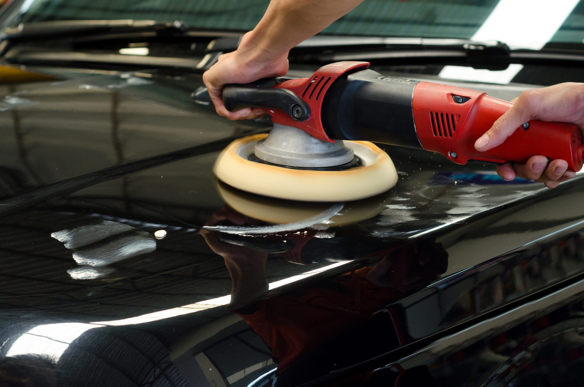 Hands with daul action polisher. polishing on car surface. hand and foam pad in blur motion from vibration of polisher machine